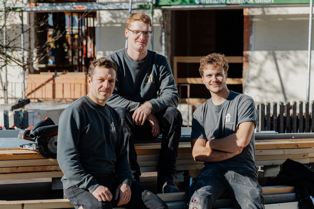 Ein Teil des Teams der Zimmerei Huber auf einem Hänger mit Holz sitzend.